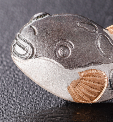  カサゴの赤は煮色という技法で生まれます。エビフライの黄金は、緊迫を施し、フグは、金銀メッキと硫化の技法が使われています。